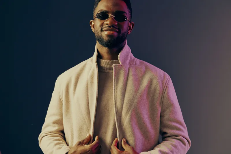Stylish young man in a beige coat and sunglasses, exuding confidence against a colorful background, perfect for fashion and lifestyle concepts