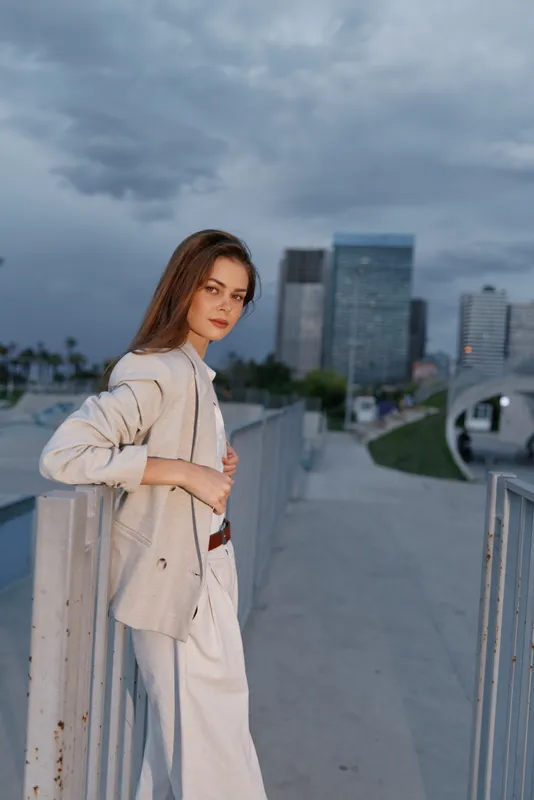 Young woman in light beige business suit standing confidently outdoors in urban cityscape under cloudy sky expressing professionalism and calm in business theme