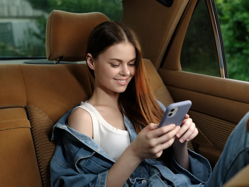 Young woman using smartphone in car, enjoying leisure time, casual outfit, natural light, happiness and relaxation, urban lifestyle, travel vibes.