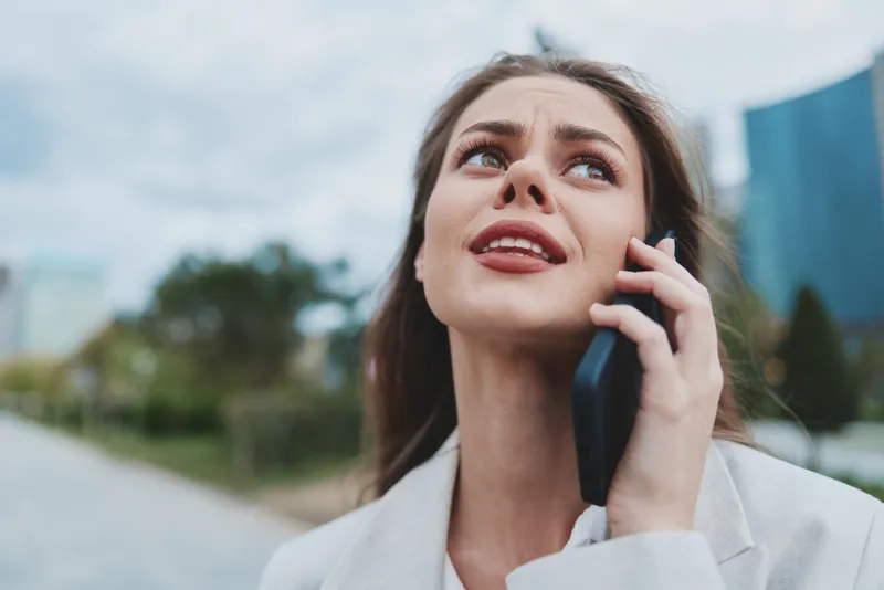 Confident businesswoman talking on phone outdoors against a modern urban background, showcasing determination and professionalism.