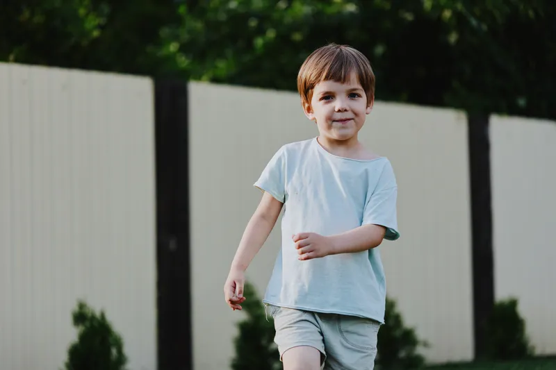 Cheerful boy running in the garden, wearing casual light blue clothes with a happy expression, showcasing childhood joy and playfulness in a vibrant outdoor setting.