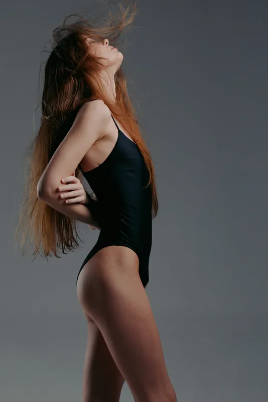 graceful woman with long hair in black swimsuit posing against gray background with soft lighting and serious expression