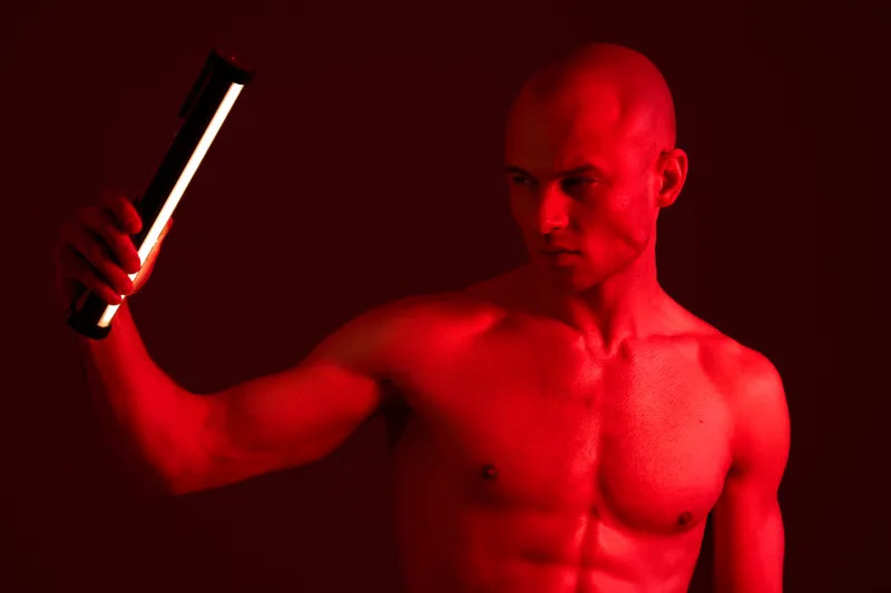 A striking image of a man holding a light in a dark environment, emphasizing the powerful contrast of light and shadow. The intense red hue adds drama to the scene.