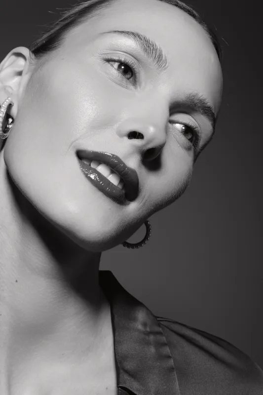 Close-up black and white portrait of a fair skinned Caucasian woman with shiny lips and earrings looking away. Concept of beauty, skincare, fashion, elegance, and confident expression.