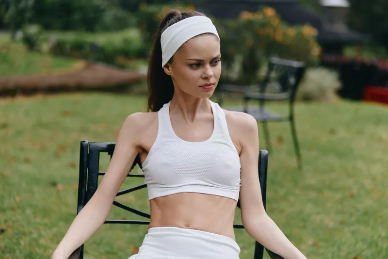 Young athletic woman in white sportswear relaxing outdoors, exuding calmness and fitness, ideal for health and wellness concepts