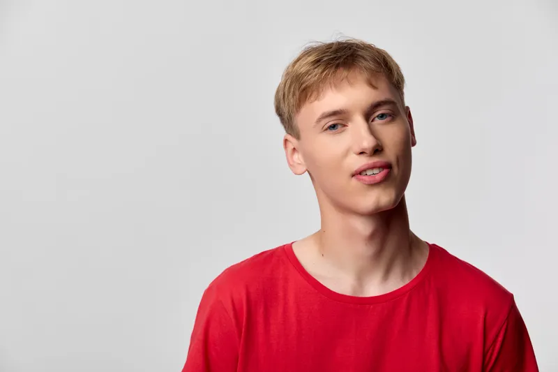 Youthful male in a red shirt smiles softly in a studio presenting casual confidence and modern lifestyle suitable for fashion marketing and stock imagery