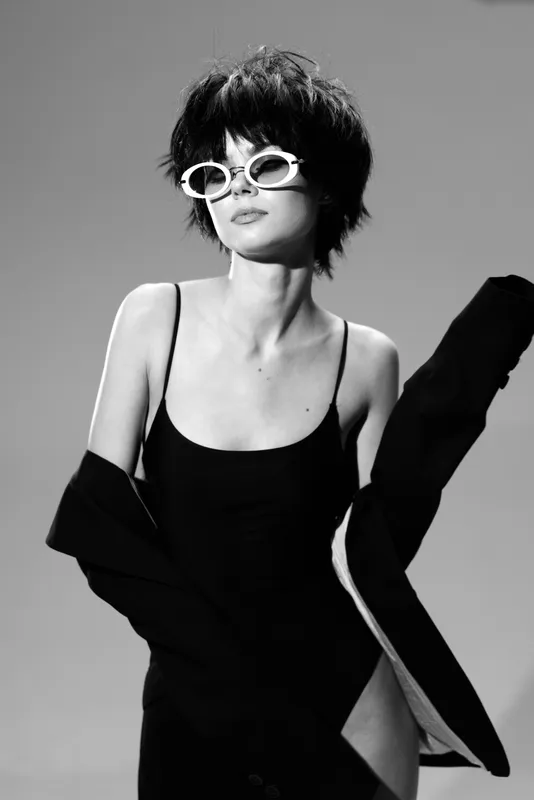 Stylish woman wearing sunglasses and a black dress in black and white, posing confidently with an elegant attitude.