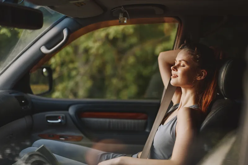 Relaxed young woman enjoying a moment of peace in her car, showcasing emotions of tranquility and contentment in a natural outdoor setting with soft lighting