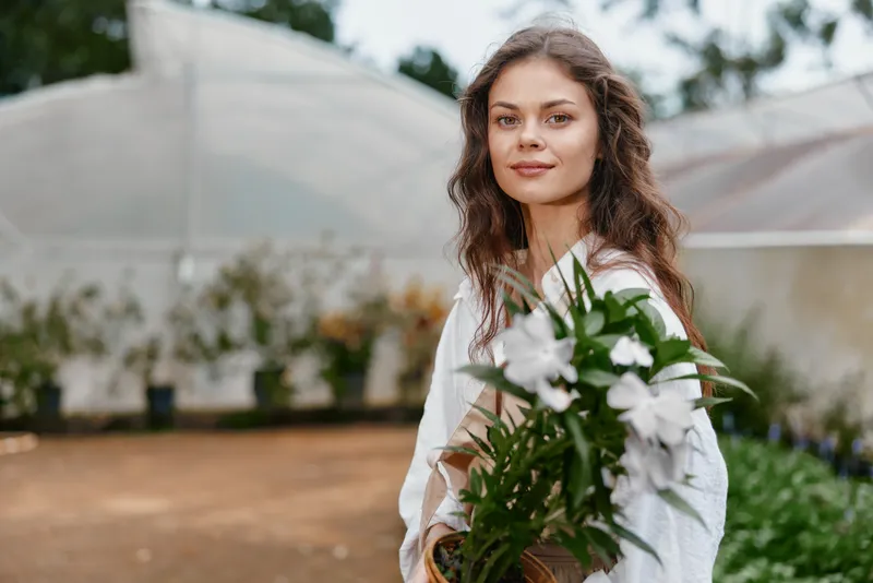 Beautiful young woman holding white flowers in a greenhouse, showcasing natural beauty and elegance, perfect for spring themes and floral arrangements