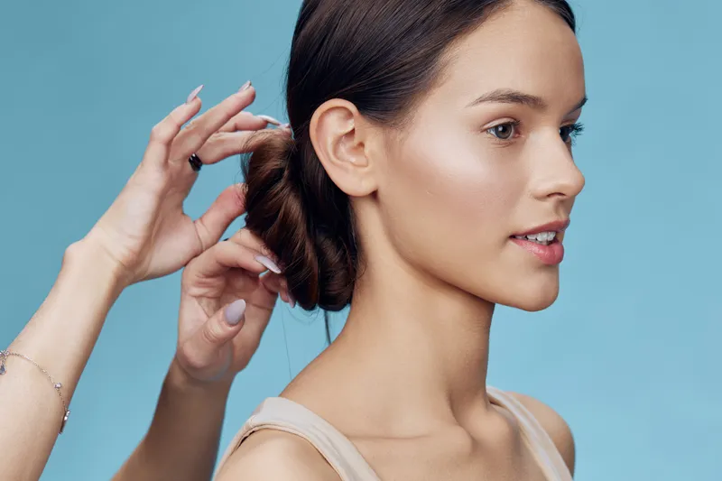Elegant hairstyle being created on a young woman with a serene expression, showcasing a soft color palette and a calm blue background, ideal for beauty and fashion themes
