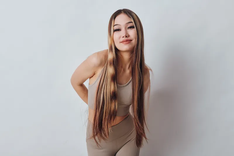 Young woman with long braided hair posing and smiling in casual beige outfit against white background. Beautiful female model with relaxed posture and confident expression.