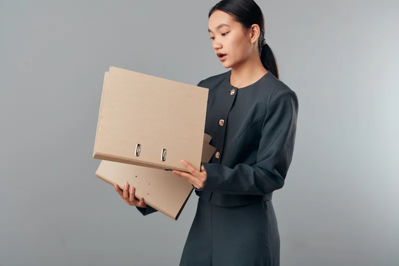 Woman holding two ring binders, standing against plain background in formal clothes for office work, organization and document management at business environment