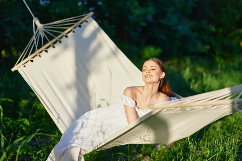 Young woman relaxing in a hammock outdoors, enjoying the sunshine and nature, with a serene expression, symbolizing peace and tranquility