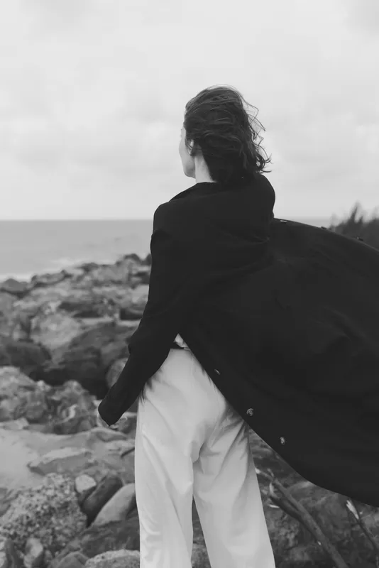 Coast wind sweeps cloak as back view figure stands on rocky shore embracing the wild outdoors and dramatic sea breeze that echoes distant horizons