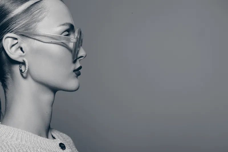 Profile of a fair skinned Caucasian woman with blonde hair wearing transparent glasses and a knitted sweater. Concept of fashion, style, and modern eyewear in monochrome.