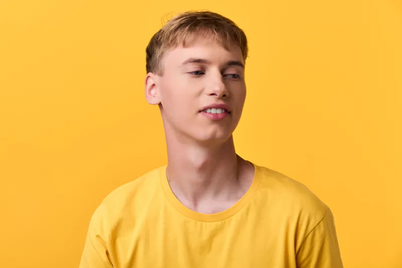 Man in yellow t shirt smiling slightly in a studio with a solid yellow backdrop, casual lifestyle image conveying warmth, brightness, and contemporary fashion vibes
