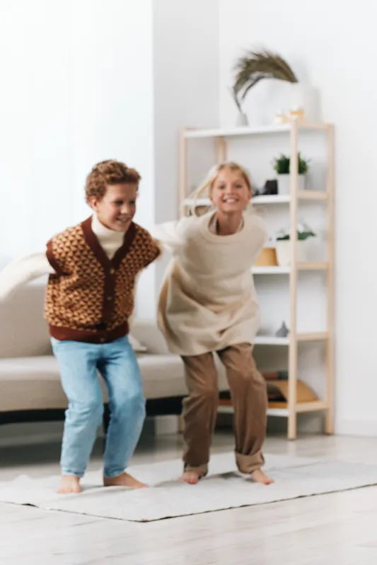 Two joyful children jump indoors in a bright living space, capturing carefree energy and playful motion as they share laughter and friendly competition.