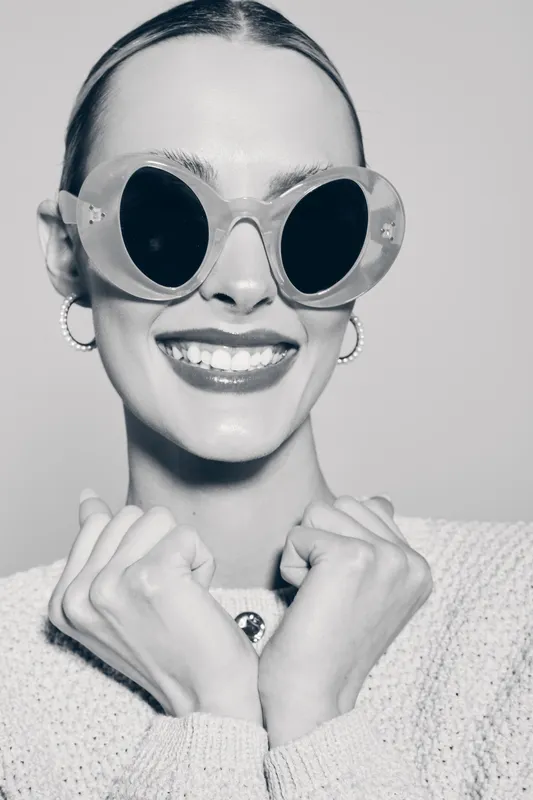 Happy Caucasian woman with fair skin wears large sunglasses and knitted sweater, smiling confidently in a studio portrait concept for fashion and lifestyle.
