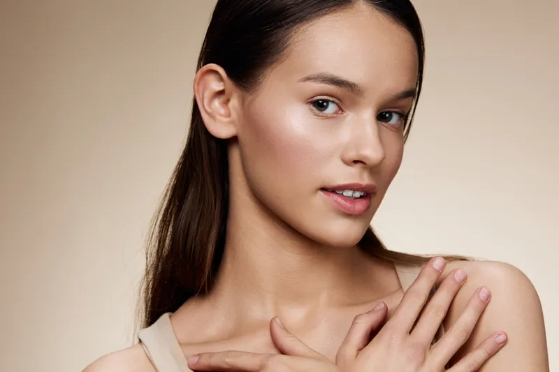A serene young model showcasing natural beauty with soft skin, wearing a simple top, against a light beige background, perfect for skincare and wellness themes