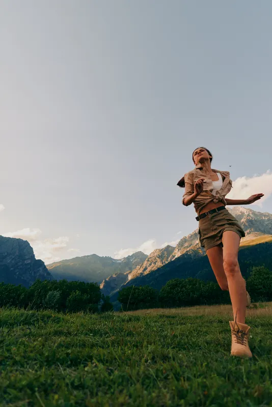 Cheerful woman outdoor lifestyle, family baby moment in a sunny mountains meadow, joyful wind, natural colors, landscape scenery, smiling pose amid green grass
