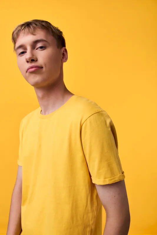 Male model in a yellow shirt stands against a vibrant yellow backdrop, showcasing casual fashion, a confident pose, and a clean studio shot with warm lighting and minimal background distraction