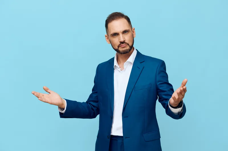 A professional man in a sharp blue suit stands against a solid colored background, projecting confident business demeanor and calm emotion in a clean isolated setting.