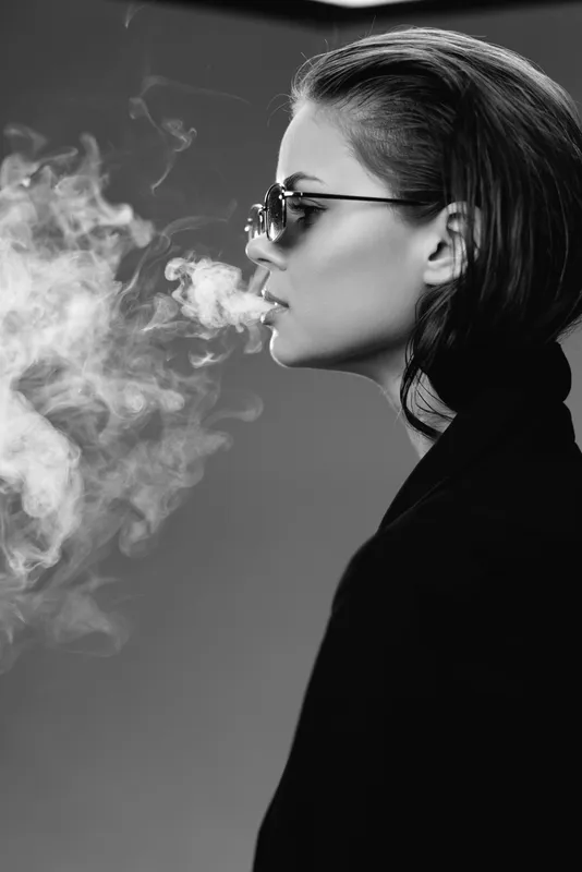 Black and white profile of a woman wearing sunglasses exhaling smoke with a calm expression