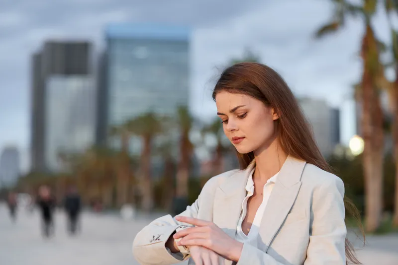 Business woman checking time with a modern city background, wearing a stylish suit, showcasing confidence and professionalism in an urban setting.
