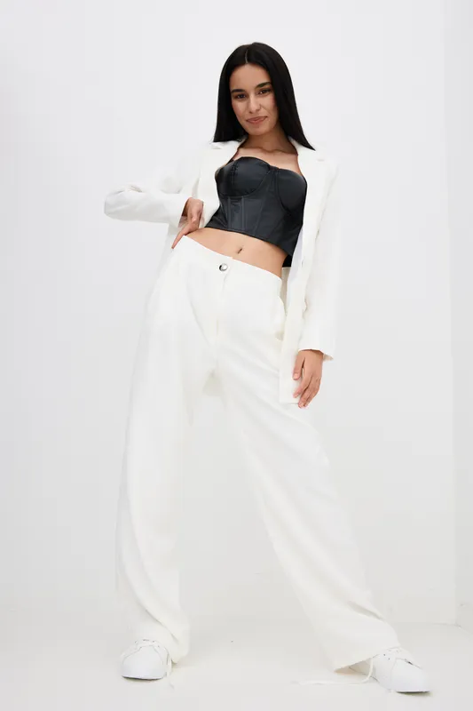 stylish woman wearing white suit and black corset top standing confidently against white background with relaxed pose and casual footwear