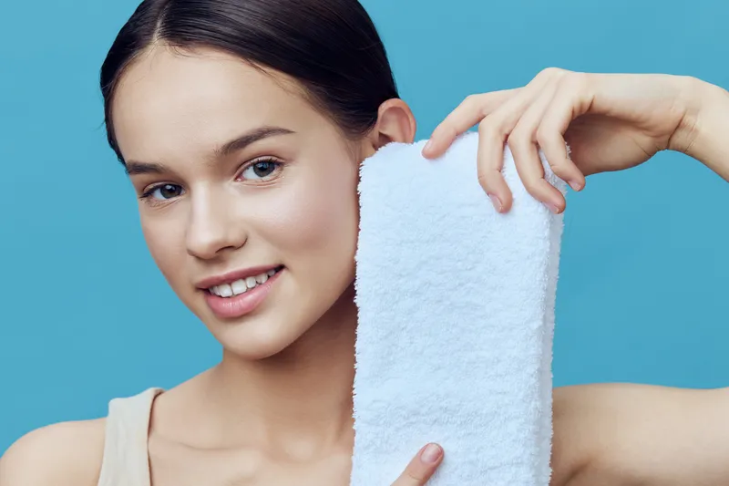 Young woman with a towel smiling on a blue background, showcasing healthy skin and beauty, ideal for wellness and skincare themes