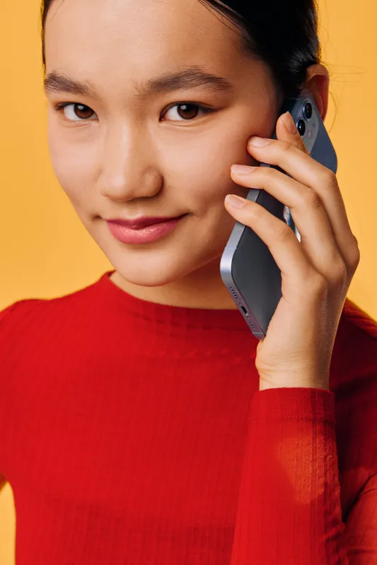 Woman wearing red top holding smartphone and talking on phone with slight smile on yellow background. Closeup portrait of young female using mobile technology communication.