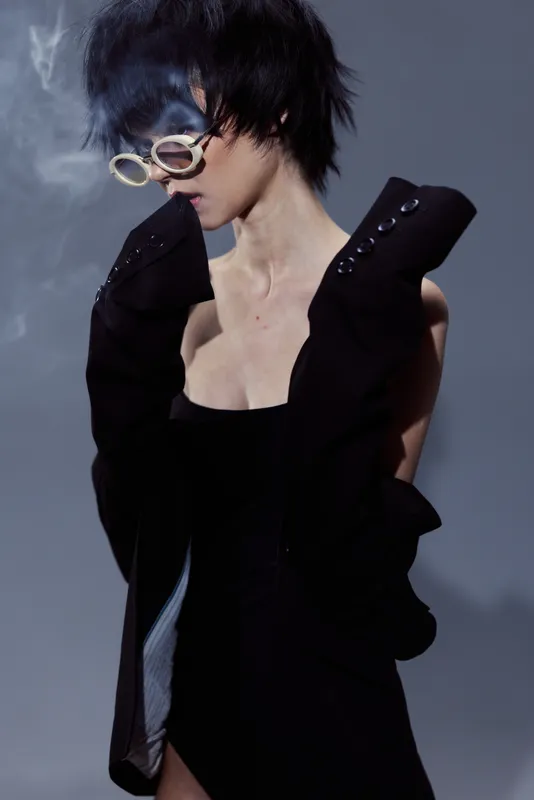 Stylish woman in black outfit wearing glasses surrounded by smoke in moody lighting