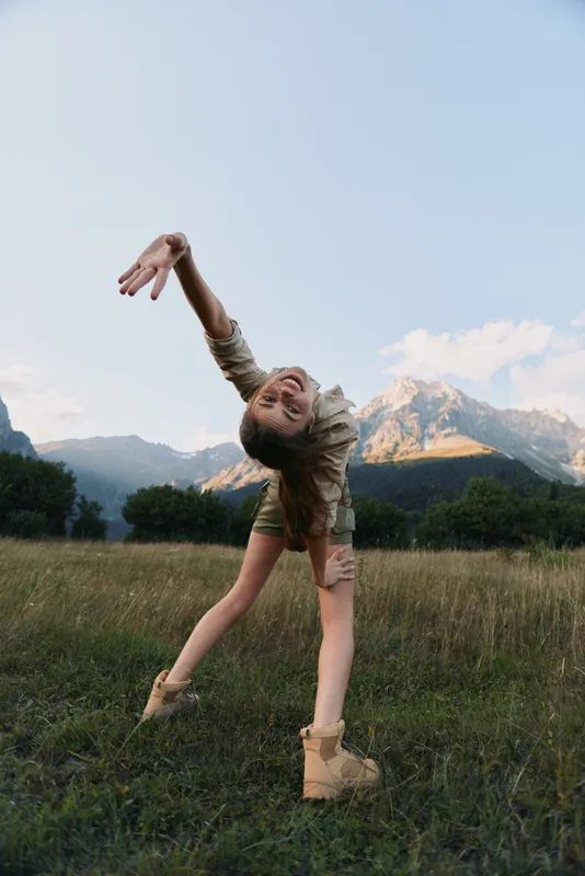 Woman dancer outdoors in a grassy field with distant mountains, expressing joy and freedom, mid motion, casual outfit, lifestyle portrait under bright sky