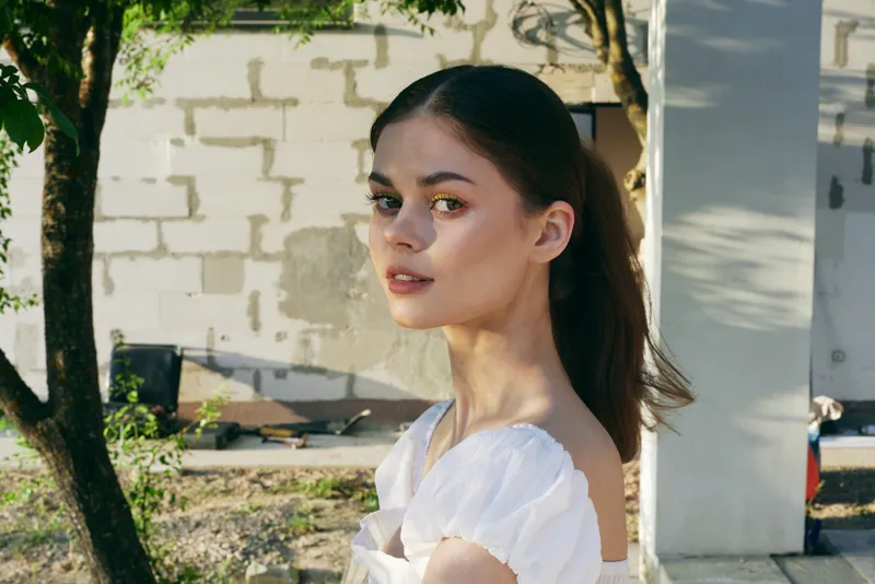 Young woman in a white dress standing outdoors, expressing serenity and confidence, surrounded by nature, ideal for seasonal lifestyle and fashion themes