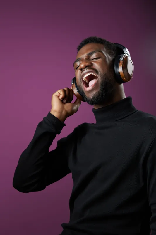 Happy young Black man singing with headphones against a purple background, showcasing joy and music enjoyment in a modern style