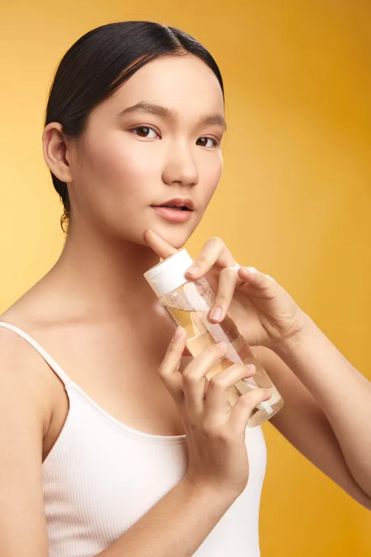 Asian woman applies skincare product in a clean studio, exuding calm confidence. This portrait highlights a gentle routine, fresh skin, and a wellness oriented beauty moment.
