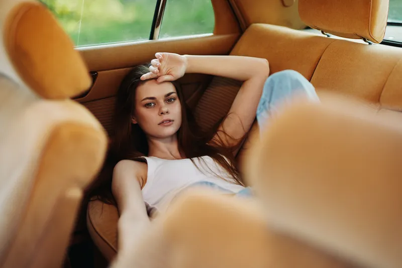 Relaxed young woman in casual outfit lounging in a vintage car, exhibiting a calm expression amidst warm orange tones, inviting a sense of nostalgia and tranquility.