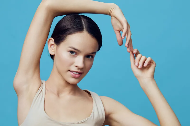 Young woman with smooth skin showcasing playful poses against a blue background, highlighting beauty, confidence, and elegance in a modern portrait style