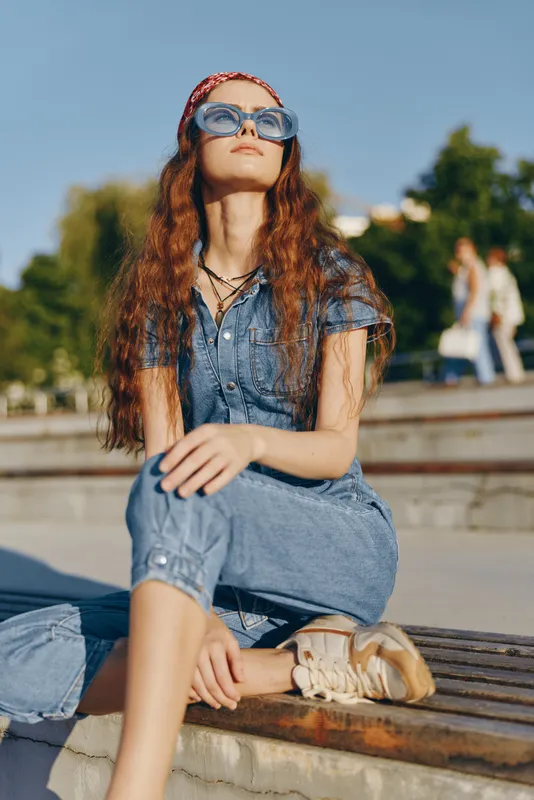 Lifestyle woman in modern boho-western denim street style, wearing sunglasses and relaxed casual outfit, captured with warm film color tones in outdoor urban setting.