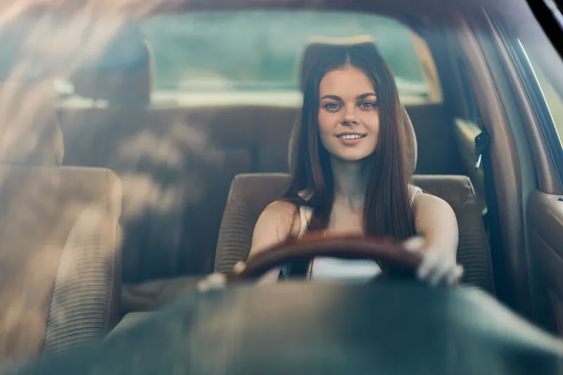 Young woman driving a car with a joyful expression, highlighting feelings of freedom and adventure in a sunny environment.
