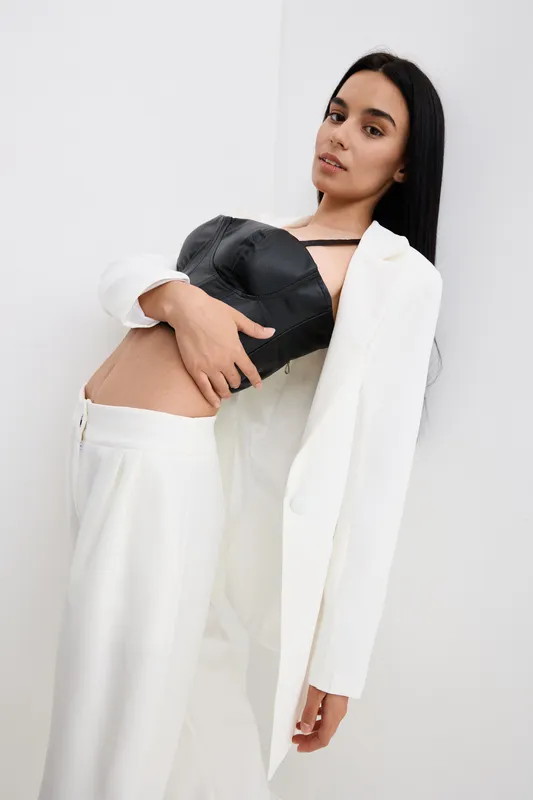 young woman posing in white suit and black leather top, stylish look with natural makeup, modern fashion style on plain light background, confident and graceful