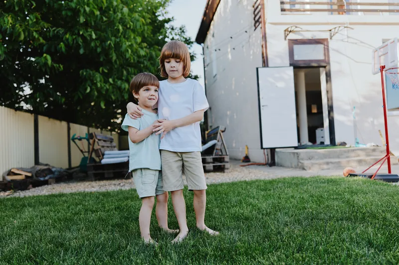 Two happy children outdoors, enjoying a sunny day in a backyard with green grass and a playful atmosphere, showcasing the joy of childhood camaraderie.