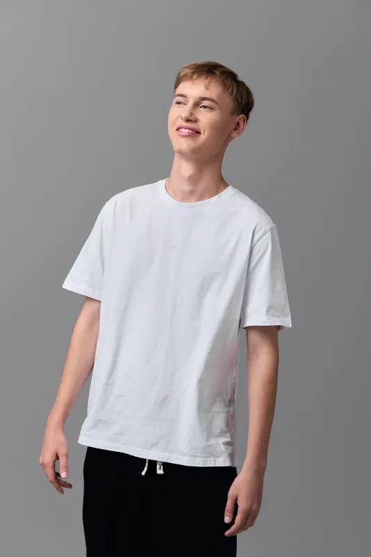 Man in a casual white t-shirt stands in a studio, smiling softly, relaxed pose suitable for lifestyle fashion and everyday wear concepts