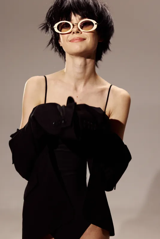 Smiling woman in black dress wearing white sunglasses with short hair in studio lighting