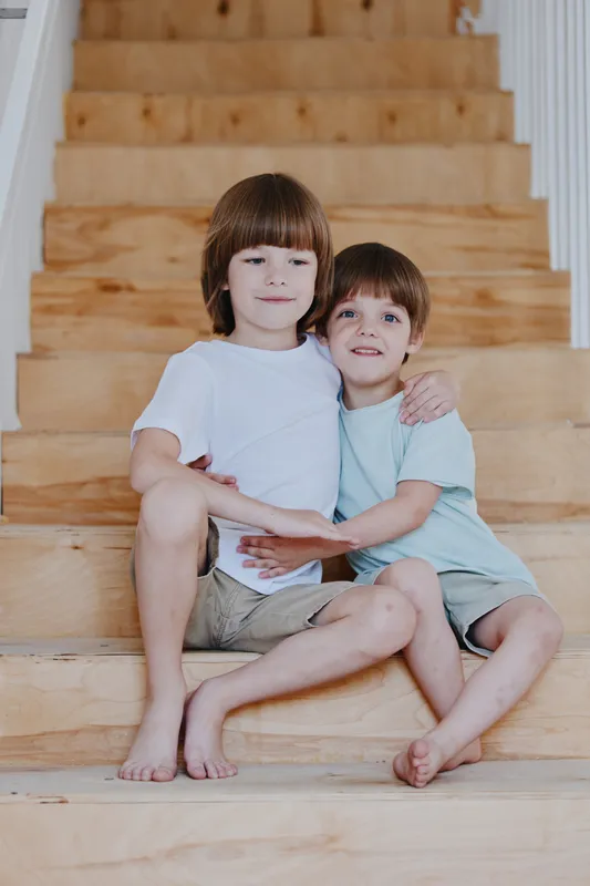 Affectionate children sitting on wooden stairs, showcasing their bond and playful spirit, reflecting warmth and innocence in a cozy environment.