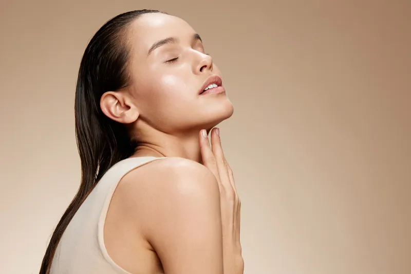 Elegant young woman with a smooth, radiant complexion showcasing skincare, expressing tranquility and confidence against a soft beige background