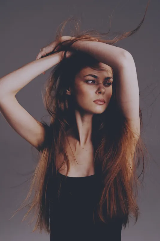 young woman with long hair posing elegantly with raised arms, natural light, moody atmosphere