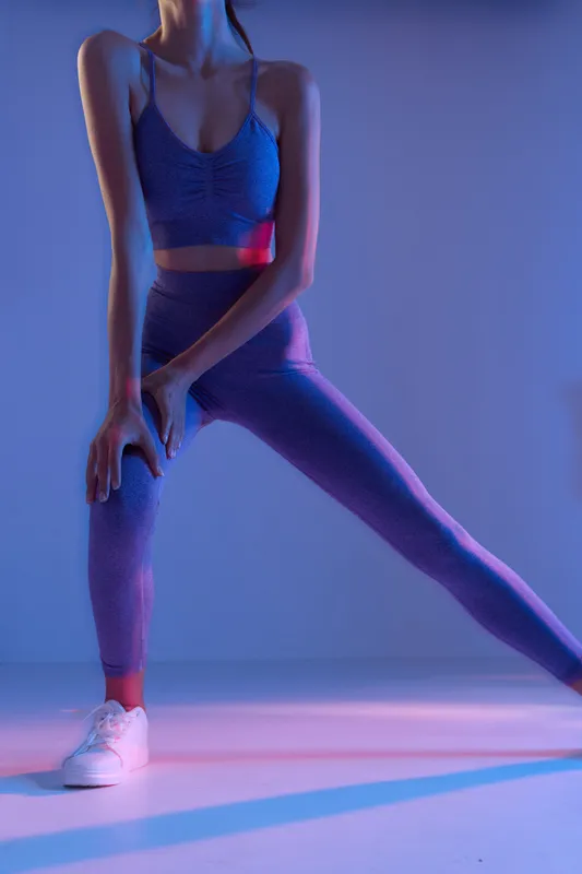 Woman sport fitness stretching in purple activewear, focused on flexibility and wellness, illuminated by soft blue and pink studio lighting.