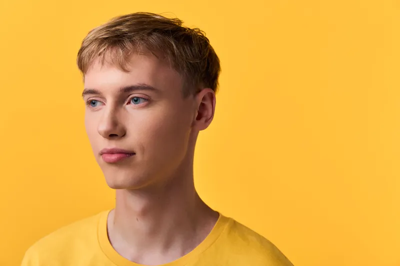 Headshot of a young man in a yellow shirt against a warm studio backdrop, conveying calm expression, subtle lighting, and a minimalist fashion vibe for lifestyle branding