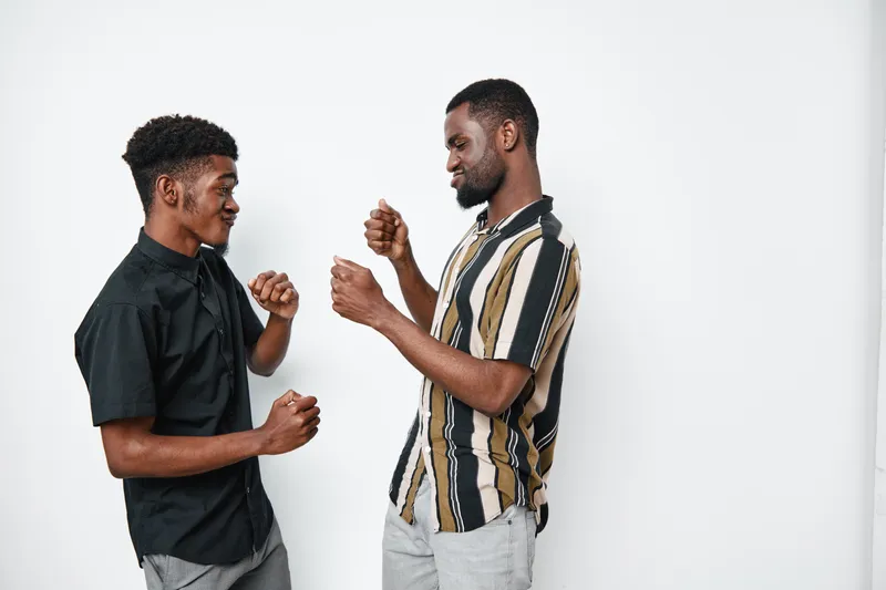 Two young black men with dark skin dancing and having fun together in casual clothes against white background. Friends enjoying music and movement indoors.